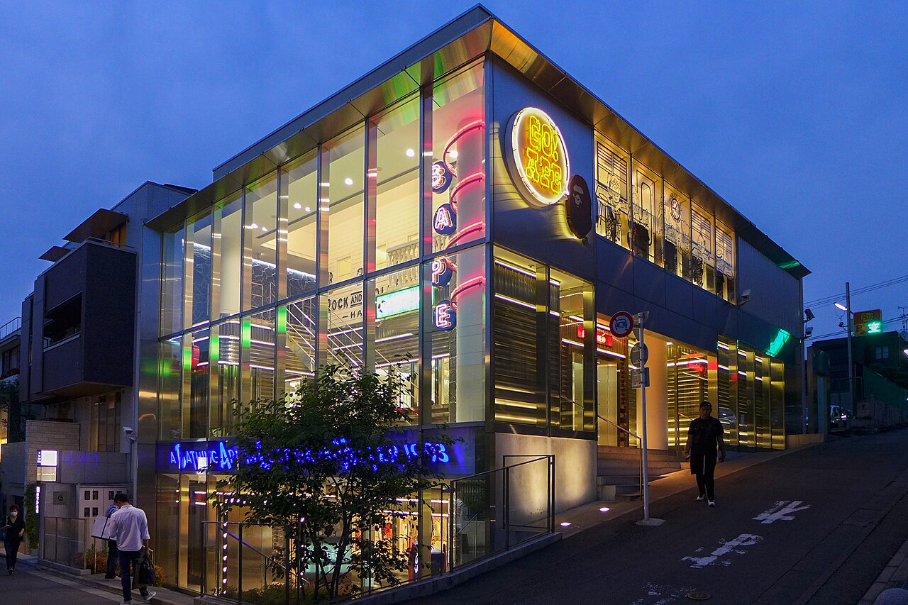 The glass fronted BAPE Store in Harajuku lit up at dusk with its neon A Bathing Ape signs