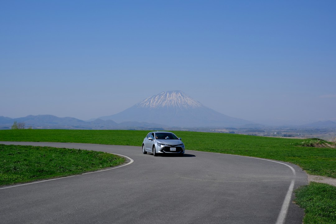 Silver hatchback on a curving country road in Hokkaido with Mount Yotei rising behind green fields
