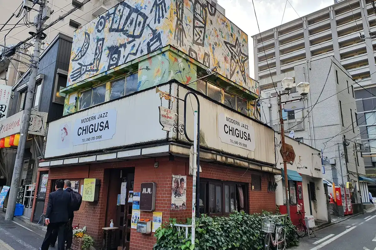 The two-storey Modern Jazz Chigusa building in Noge, Yokohama, with a painted mural on the upper wall, white signs reading Modern Jazz Chigusa and a red brick ground floor