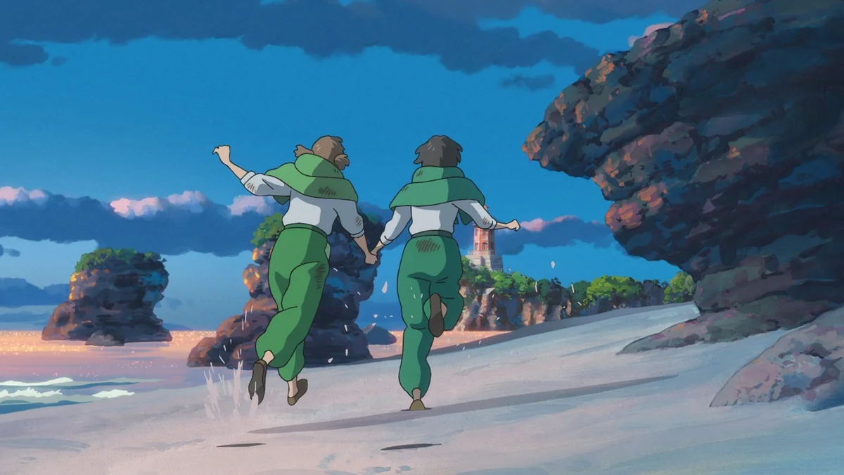 Two girls in green capes and trousers run along a white beach towards tall rock formations under a deep blue sky.