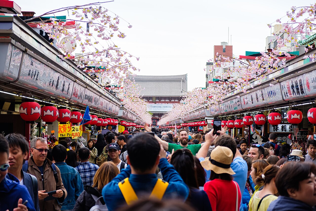 Dense crowds on Nakamise shopping street in Asakusa in April, with cherry blossom decorations above the shops