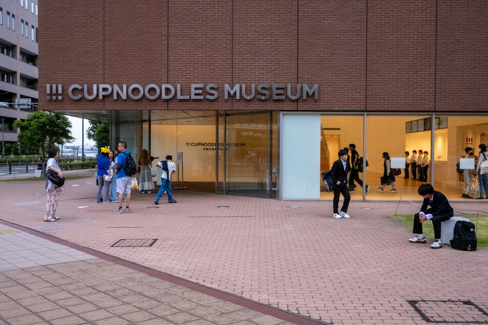 Visitors outside the entrance of the Cupnoodles Museum in Yokohama, a red brick building with the museum name above the glass doors
