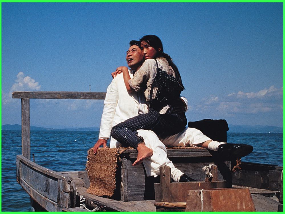 Colour still from Dr. Akagi (1998): a man in a white suit and a young woman sit together on a wooden boat at sea