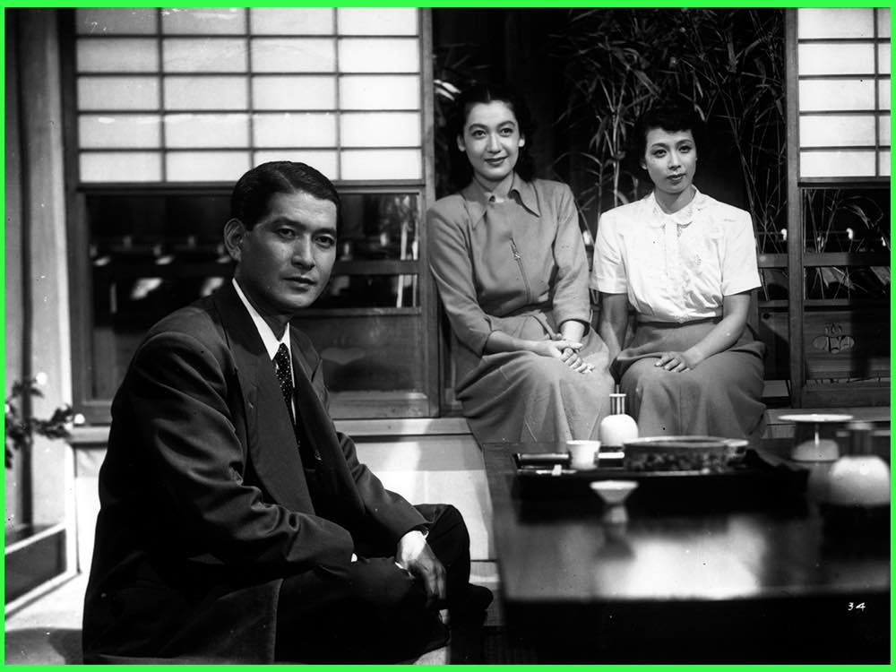 Black and white still from Early Summer (1951): a man in a suit and two women sit on a veranda overlooking a garden