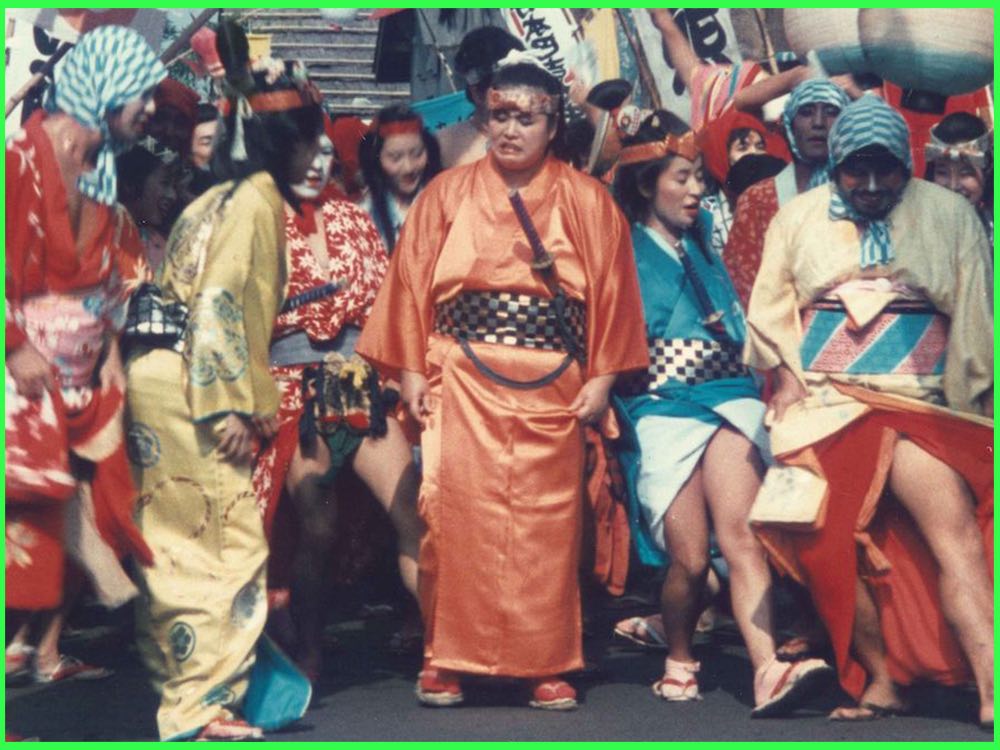 Colour still from Eijanaika (1981): a crowd of dancers in bright kimono and painted faces fill a street