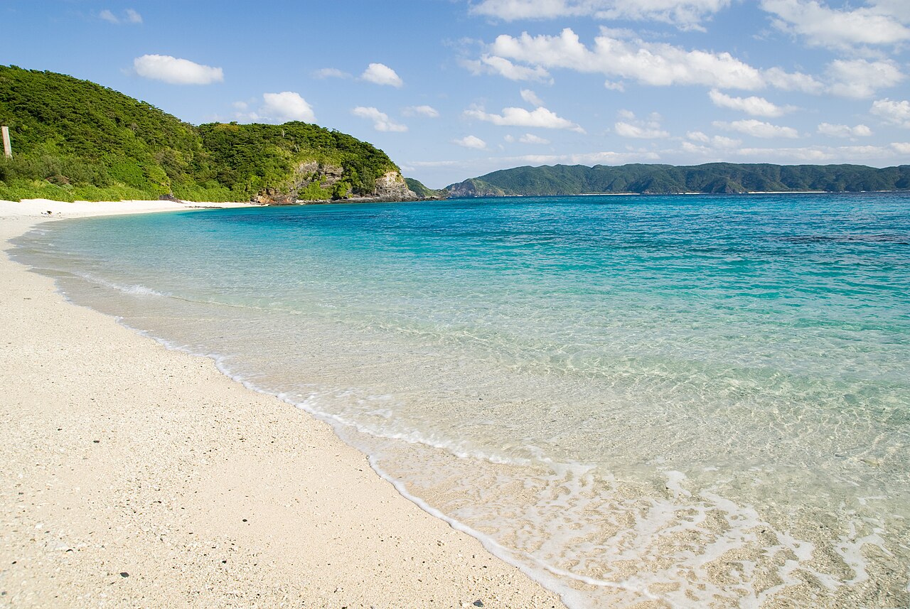 Clear turquoise water lapping the white sand of Furuzamami Beach on Zamami Island, with green headlands behind