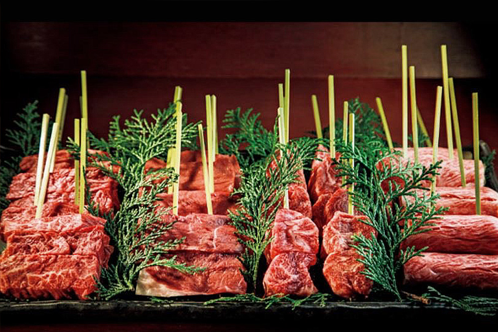 Blocks of marbled wagyu beef laid out with straw and cypress sprigs at Ginza Niku Okazaki