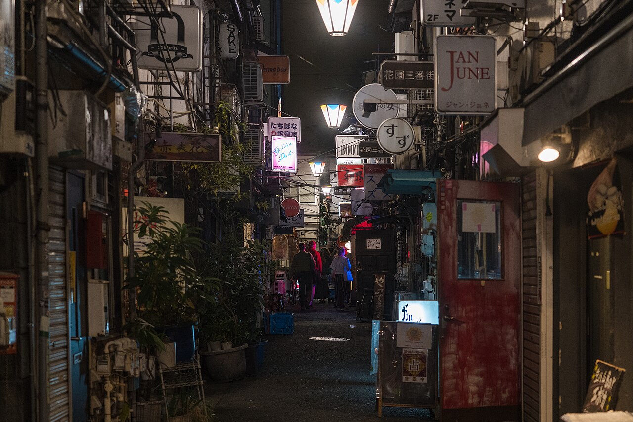 A narrow lane of tiny bars in Shinjuku Golden Gai at night, lit by small signs and lamps