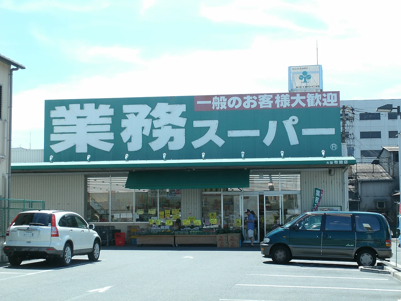 Green Gyomu Super sign above the Fuse branch in Higashiosaka, with a red banner welcoming general shoppers and cars parked out front