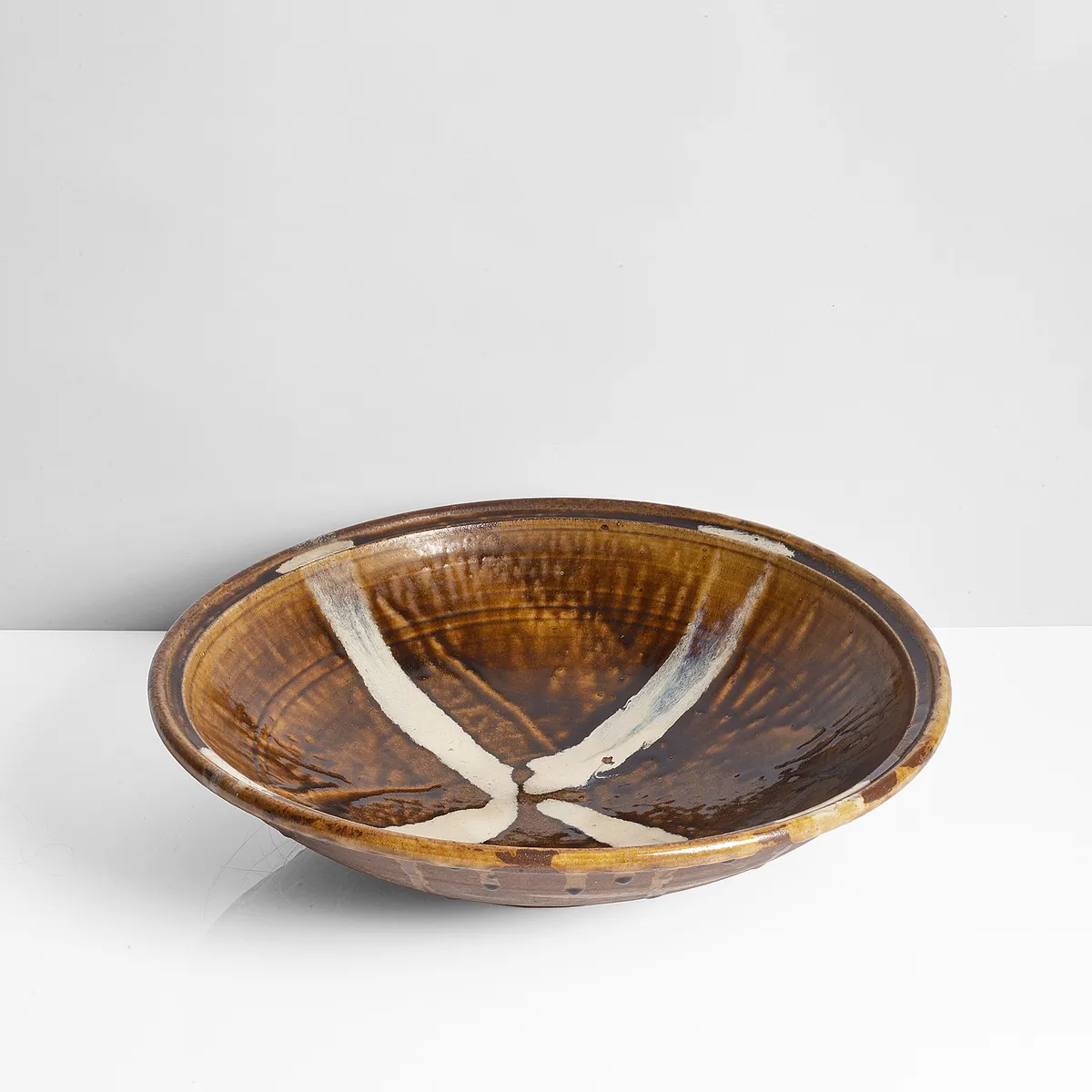 Wide stoneware bowl with amber glaze running over iron and cream pours forming a cross in the well
