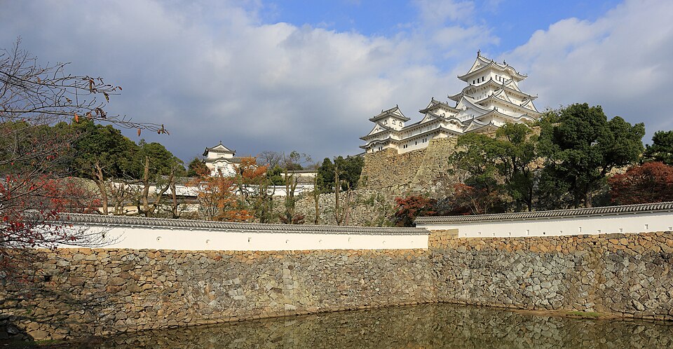 The white keep of Himeji Castle rising above its stone walls and moat in autumn