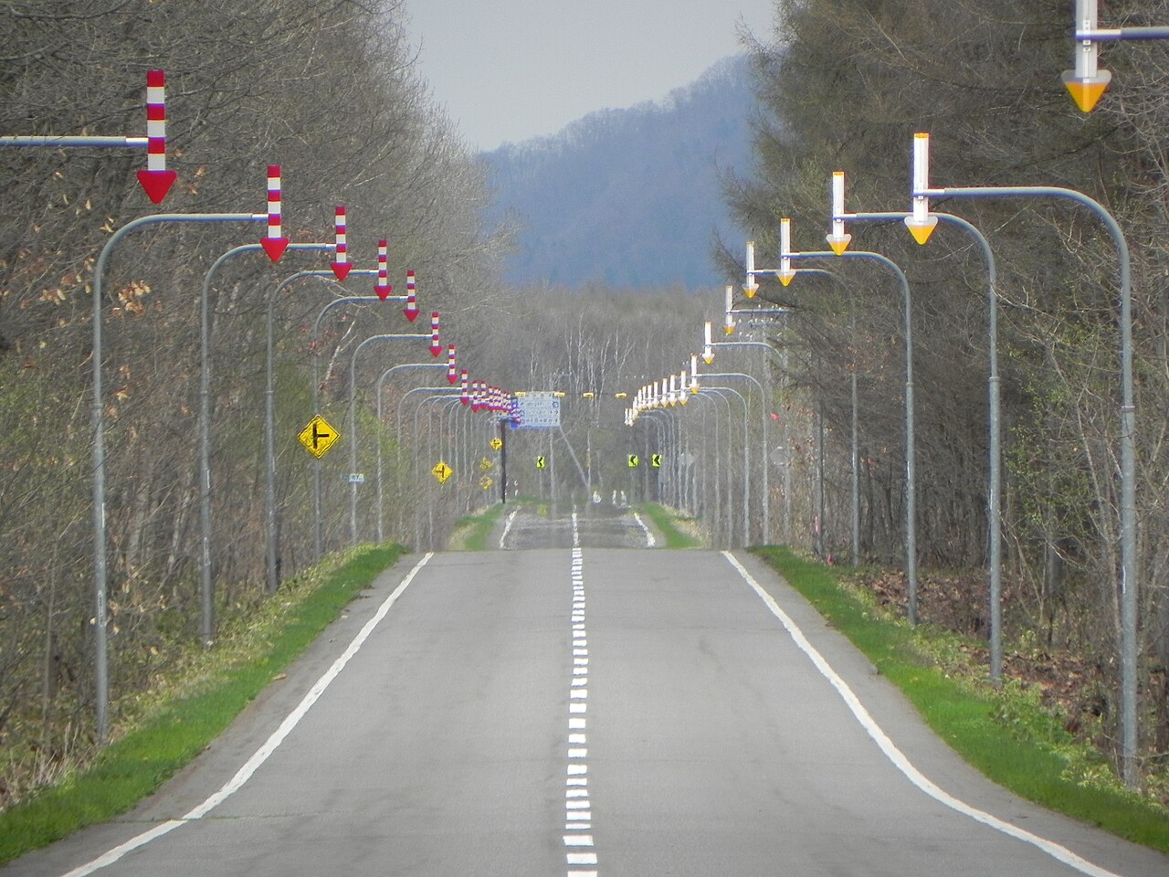 Straight rural road in Hokkaido lined with red and white arrow snow poles that mark the road edge when snow is deep