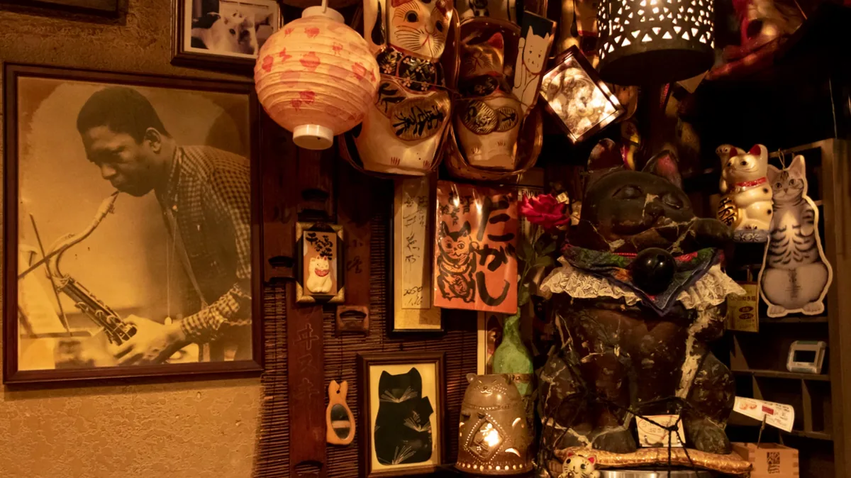 Framed photograph of a saxophonist beside a wall crowded with lucky cat figurines, paper lanterns and jazz memorabilia in a Tokyo jazz bar