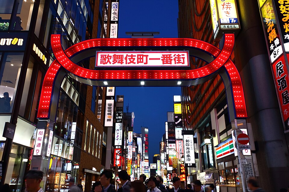 The red illuminated Kabukicho Ichibangai gate in Shinjuku at dusk, with neon signs lining the street behind it