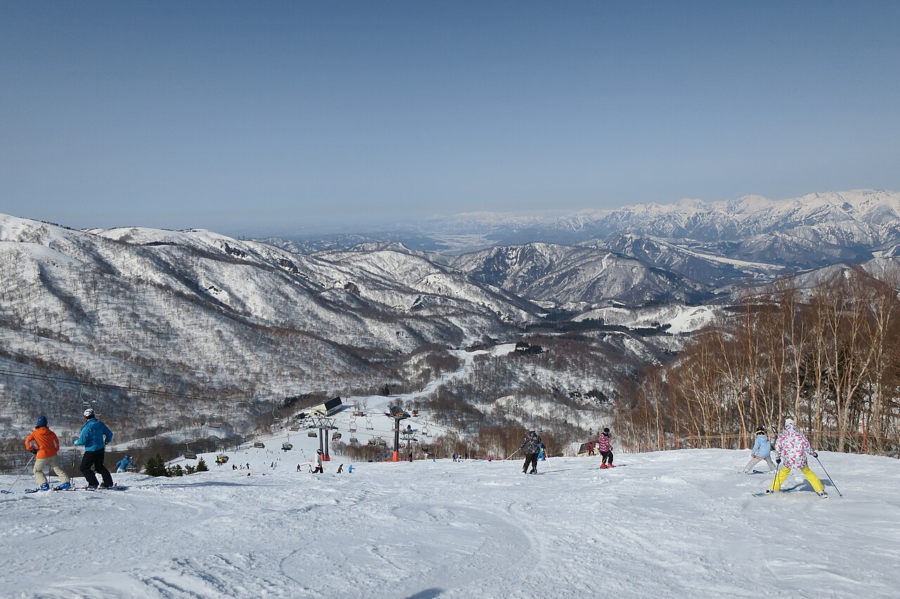 Skiers on a wide groomed run at Kagura Ski Resort in Yuzawa, with chairlifts and snowy mountains beyond