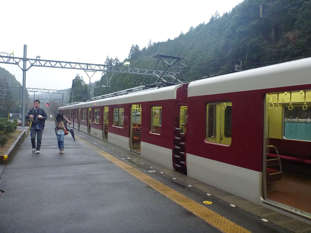 Red and cream Kintetsu train waiting at the platform of Kintetsu Yoshino Station, with wooded hills behind