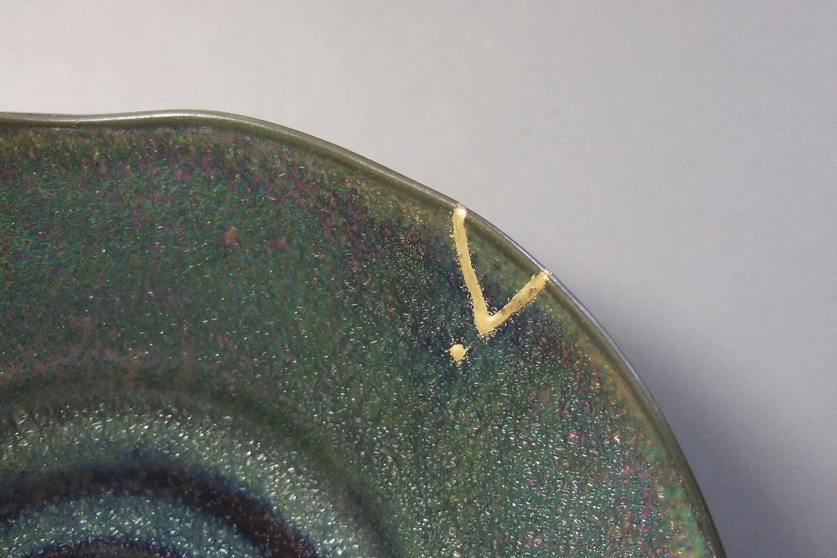Close-up of the rim of a green glazed plate where a small chip has been filled and outlined in gold