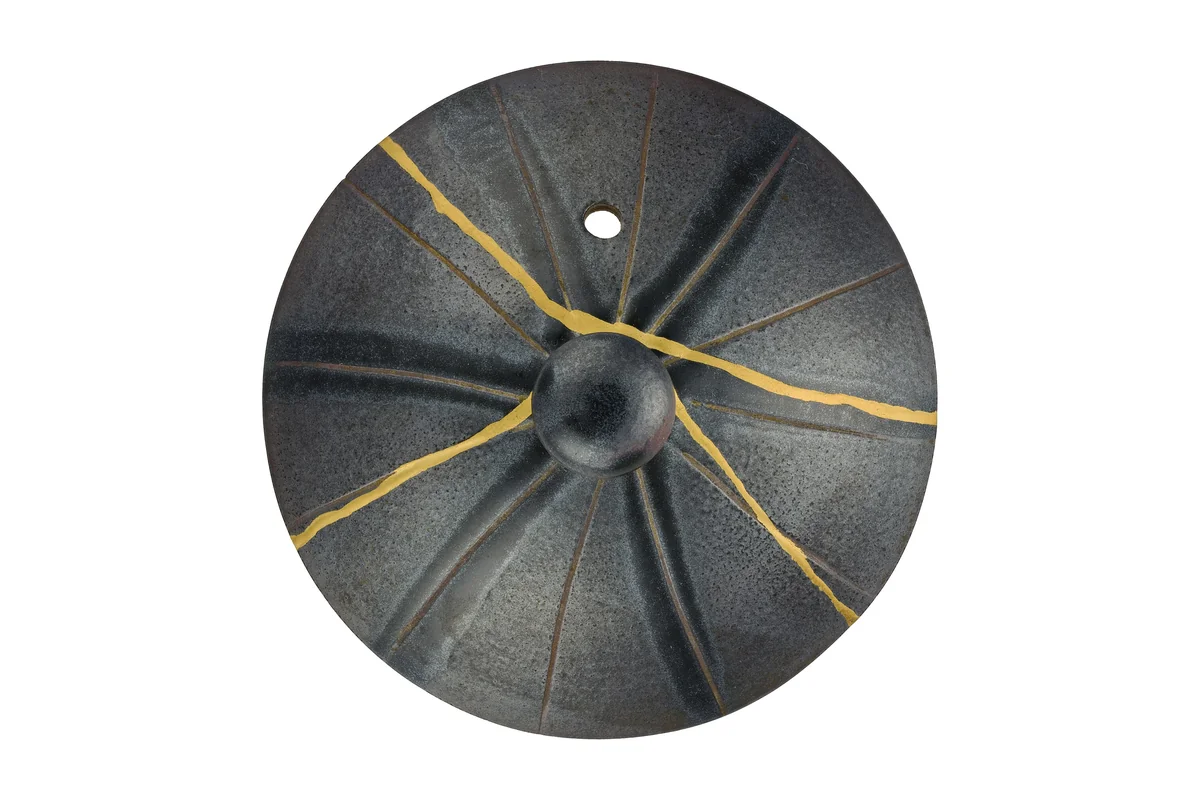 The dark grey lid of a Japanese side-handled teapot, broken into pieces and rejoined with bright gold seams radiating from the knob