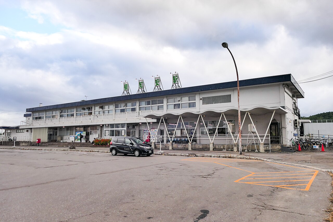 The low white station building of JR Kutchan Station in Hokkaido, with a taxi parked in front
