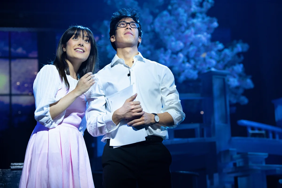 Mia Kobayashi and Zheng Xi Yong as Kaori and Kosei looking up under cherry blossom on stage