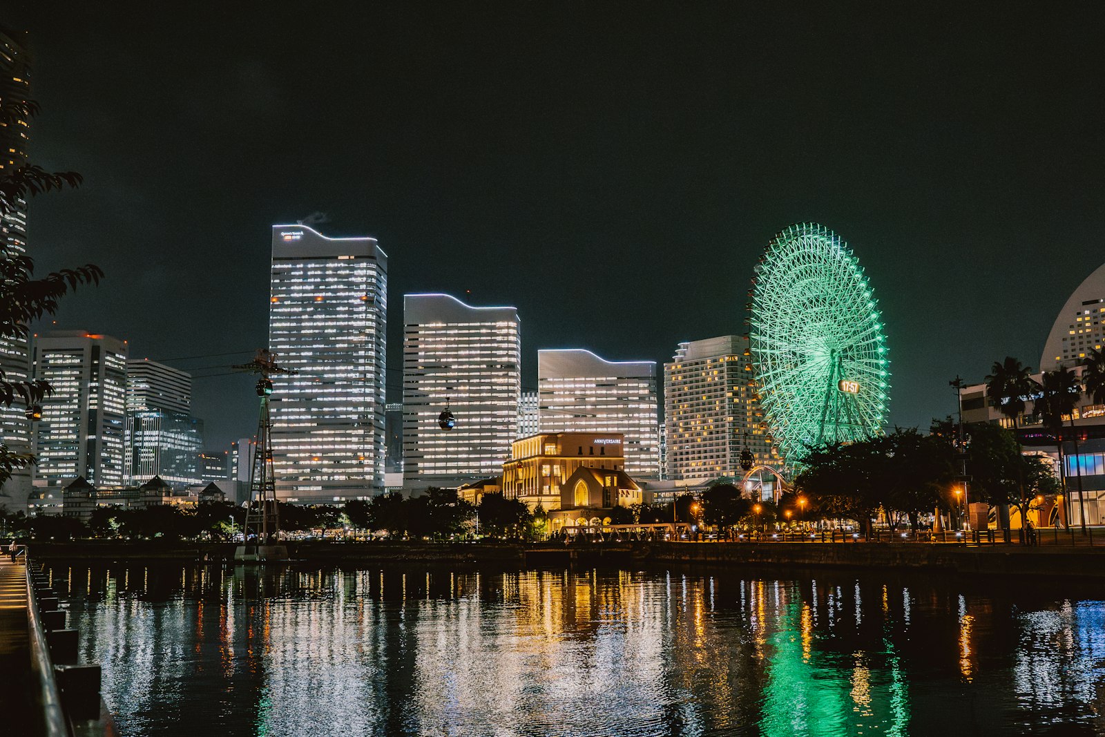 Minato Mirai 21 skyline at night, with the green lit Cosmo Clock 21 Ferris wheel reflected in the water