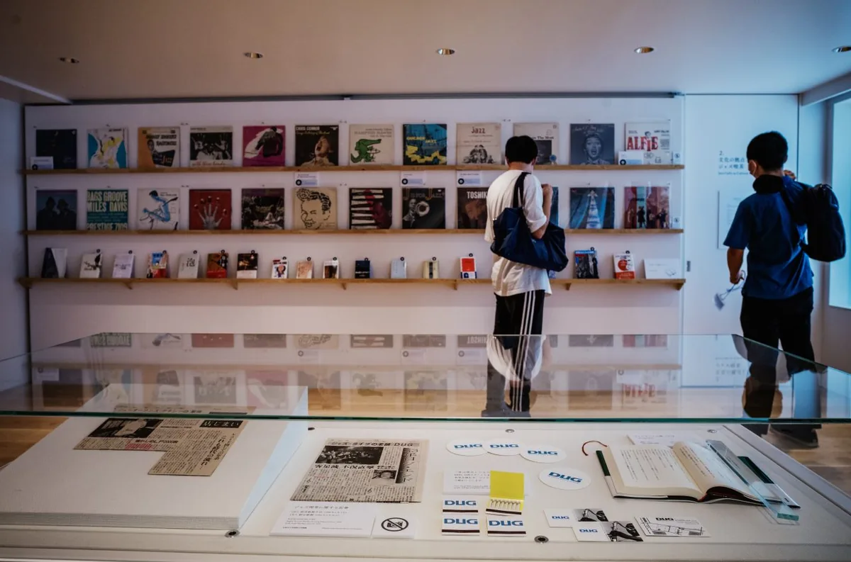 Visitors looking at a wall of jazz record sleeves above a display case of DUG matchboxes and magazine cuttings at the Haruki Murakami Library
