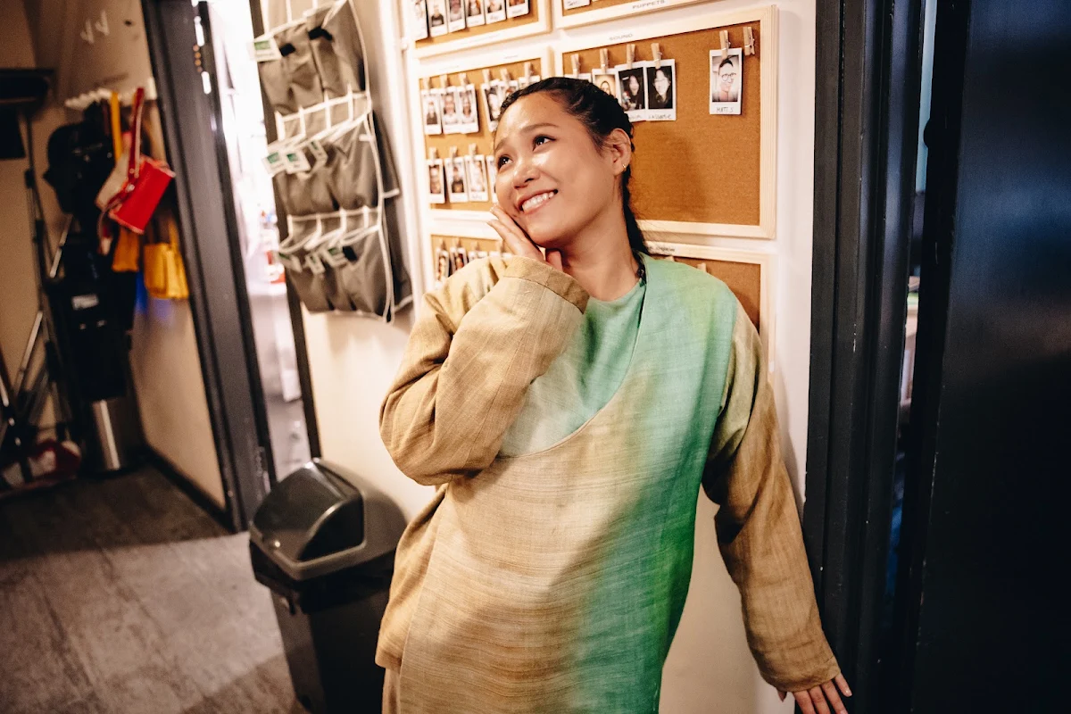 Ai Ninomiya in a green and oatmeal costume smiling in a backstage corridor
