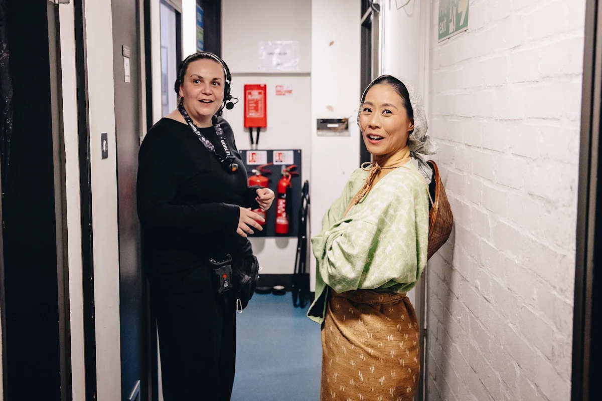 Natsumi Kuroda in a pale green costume and headscarf in a backstage corridor beside a crew member wearing a headset