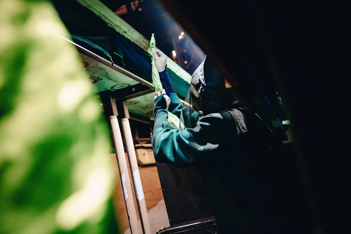 A performer in dark clothing handling a piece of green scenery in the shadows of the wings