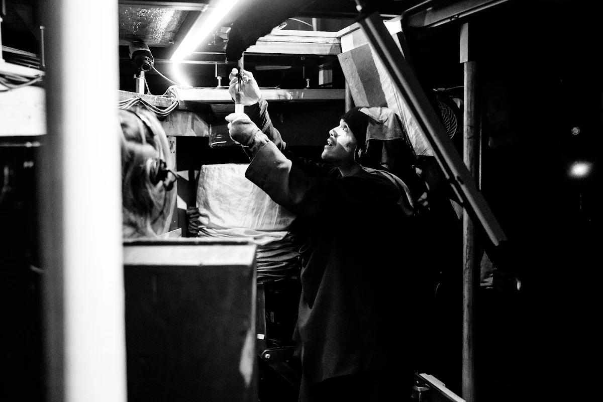 Black and white photograph of Victor Itang reaching up to work a piece of equipment in the wings