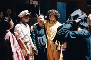 Victoria Chen, Steven Nguyen, Chui Yen and Helen Chong laughing together in costume in the wings, with a hooded puppeteer beside them