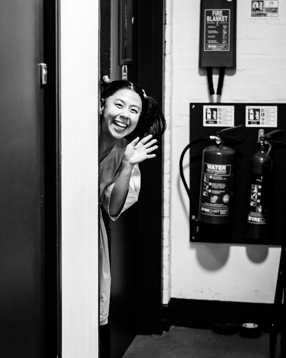 Victoria Chen smiling and waving as she leans out of a backstage doorway