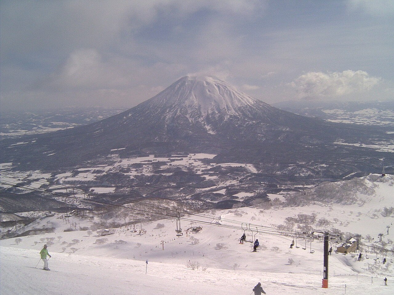 Skiers on the upper slopes of Niseko Grand Hirafu with snow-capped Mount Yotei across the valley