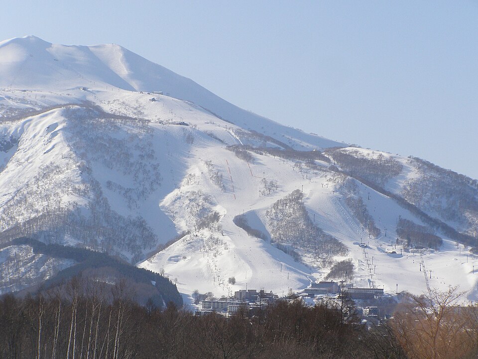 Ski runs and lifts of Niseko Grand Hirafu below the snowy summit of Mount Niseko Annupuri, with resort buildings at the base