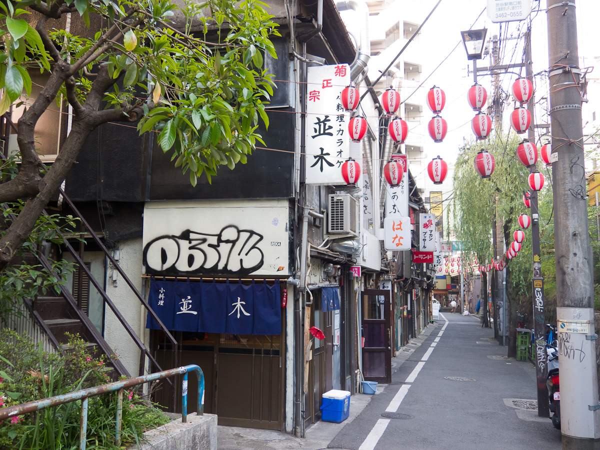 The lane of Nonbei Yokocho in Shibuya by day, with small bar fronts and red paper lanterns along one side