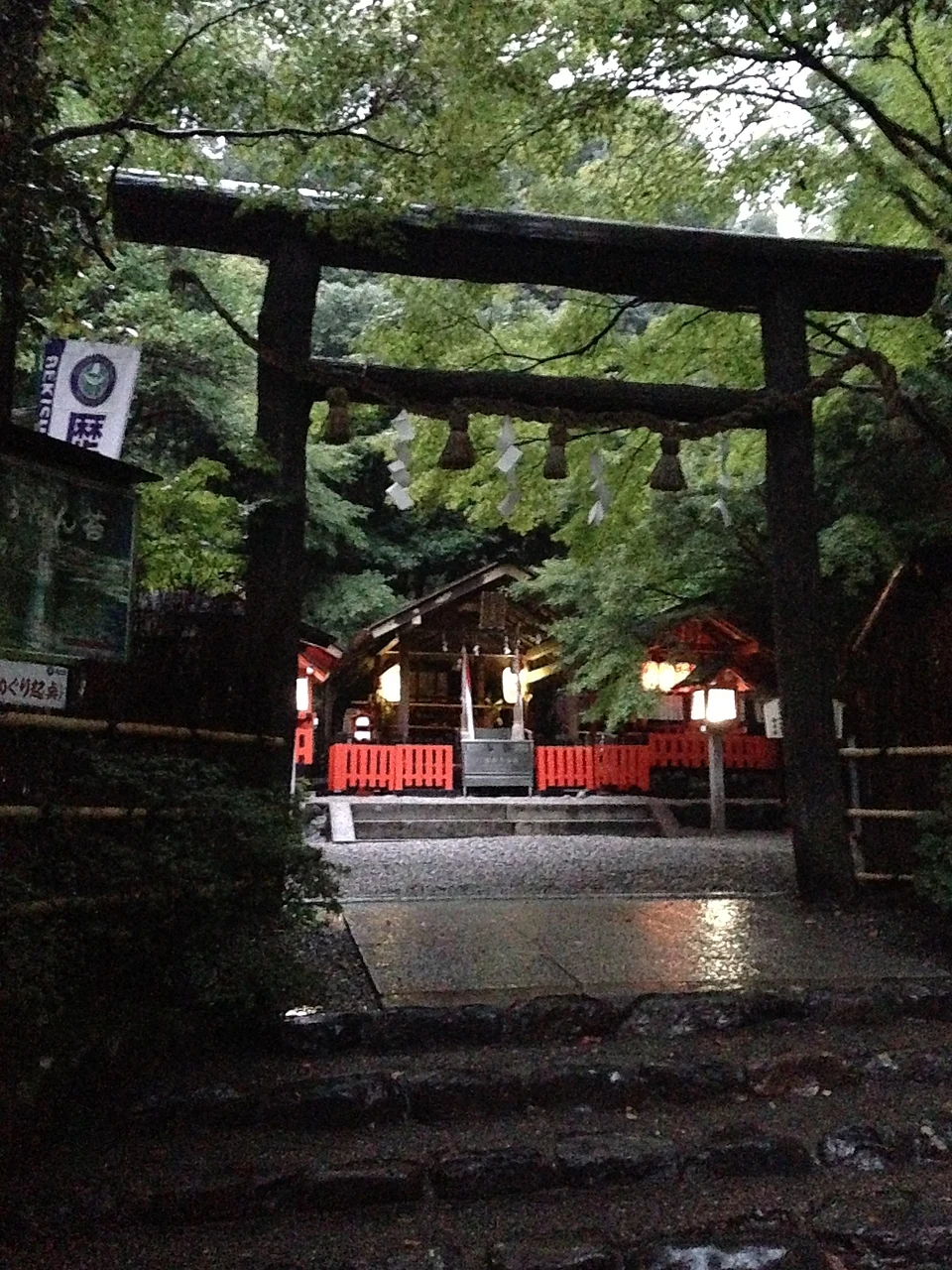 Black unbarked wooden torii gate at the entrance to Nonomiya Shrine in Arashiyama, Kyoto, with the shrine hall and its red fence behind