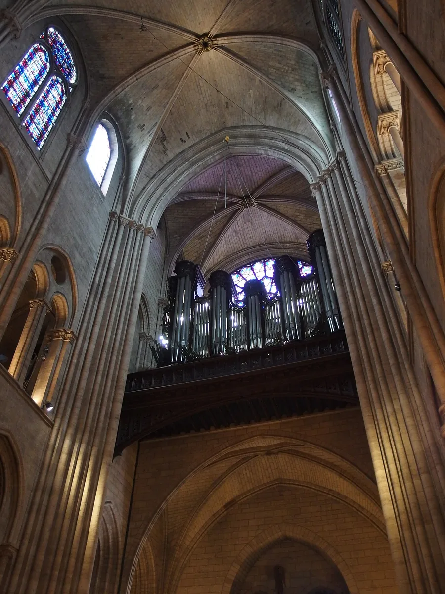 The great organ of Notre-Dame de Paris seen from the nave, its pipes set high beneath the rose window and Gothic vaulting.