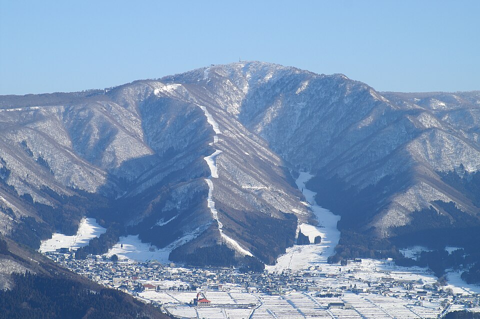 Nozawa Onsen village in the snow at the foot of the mountain, with ski runs climbing the slopes above it