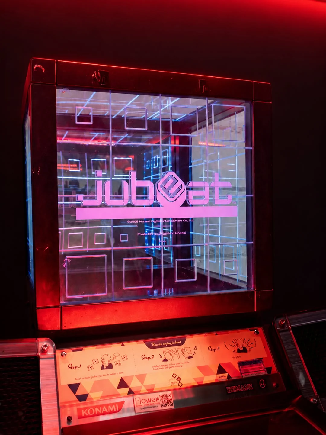 A Konami jubeat cabinet with its glowing grid of square touch panels showing the jubeat logo in pink, under red light