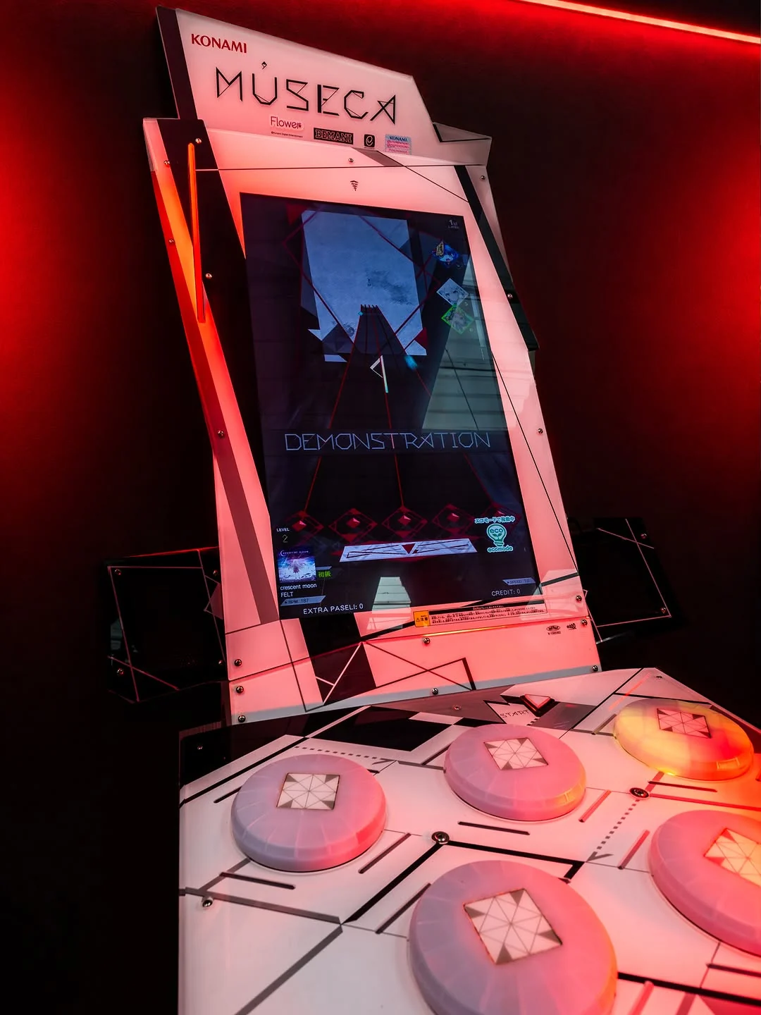 A Konami Museca cabinet with a row of round white spinning controllers in front of an angled screen, under red light