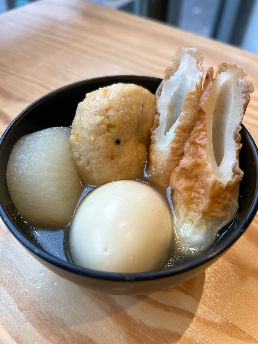 A bowl of oden in clear broth with daikon radish, a boiled egg, a round fishcake and a tube of chikuwa