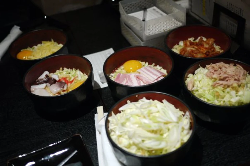Bowls of raw okonomiyaki batter with shredded cabbage, egg and toppings ready to be mixed and cooked by diners at a Tokyo okonomiyaki restaurant