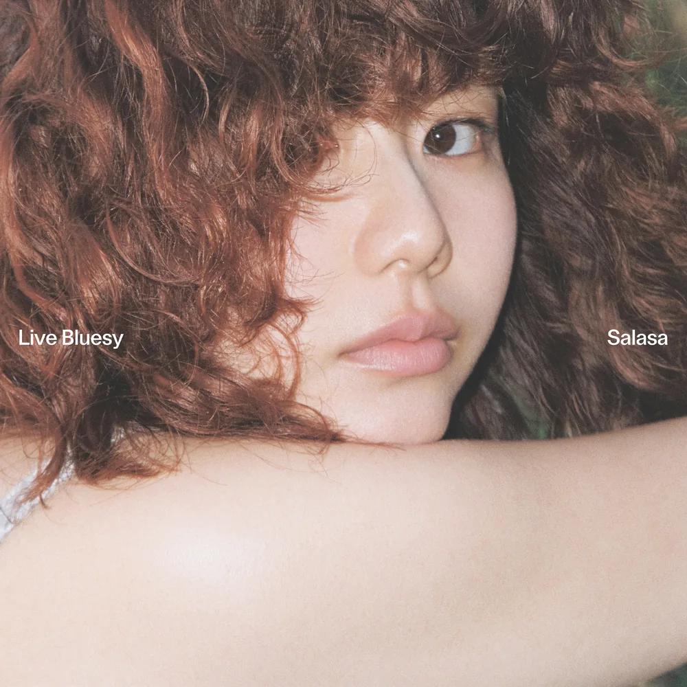 Close up of Salasa with curly auburn hair, resting her cheek on her arm and looking at the camera