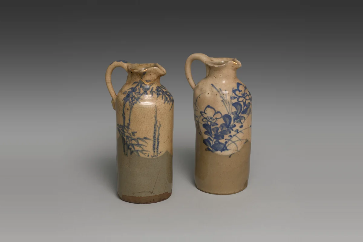 A pair of tall stoneware sake pourers with small spouts and handles, painted in blue with bamboo and bellflowers, one with thin gold repair lines