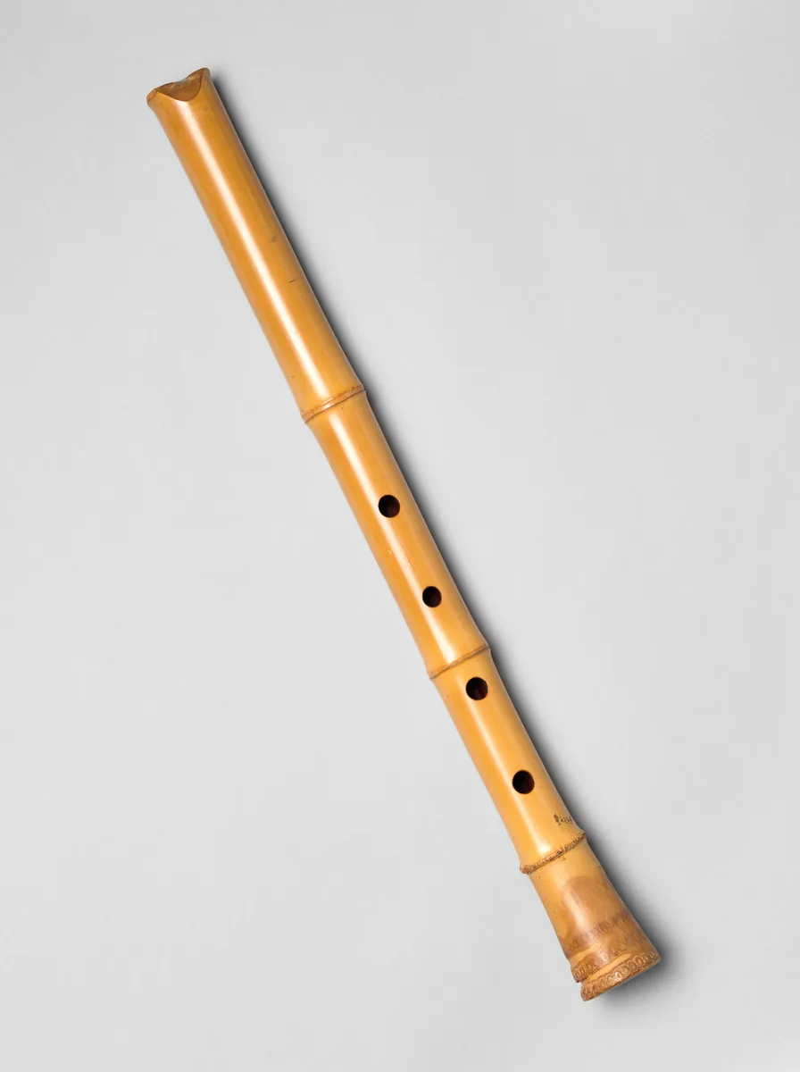 A plain bamboo shakuhachi flute with four visible finger holes, photographed against a pale grey background.