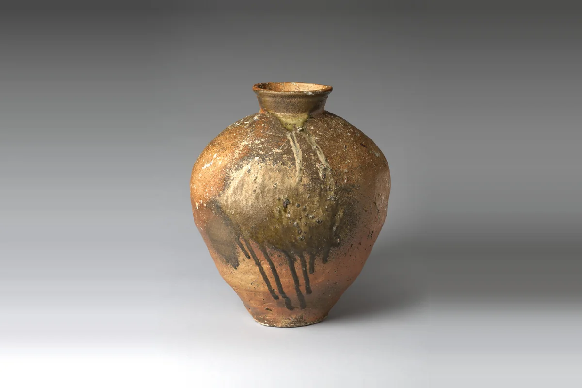A large Shigaraki stoneware storage jar with a flared mouth, its orange body streaked with drips of green-brown natural ash glaze running down from the shoulder