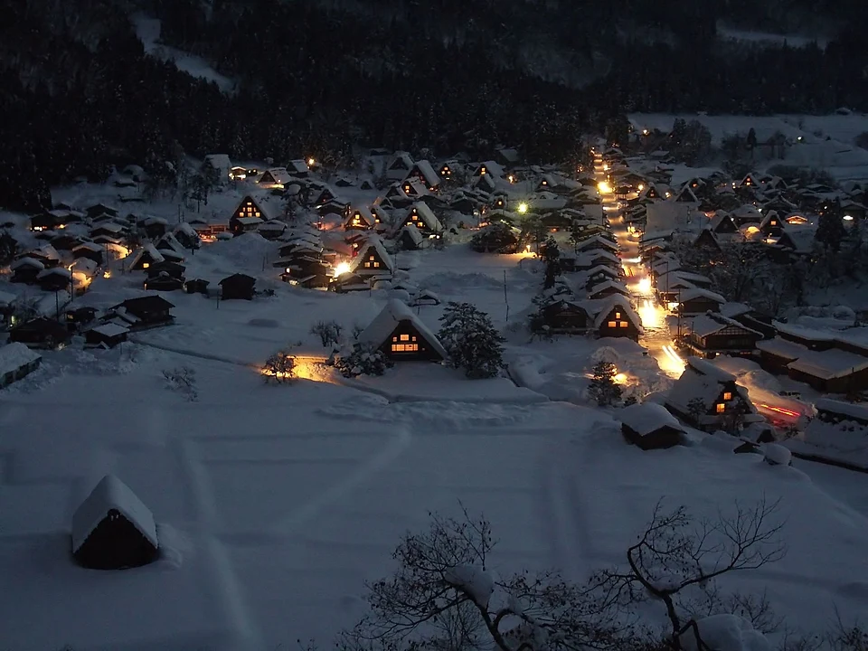 Snow covered gassho-zukuri farmhouses in Ogimachi, Shirakawa-go, with lit windows at dusk seen from the observatory