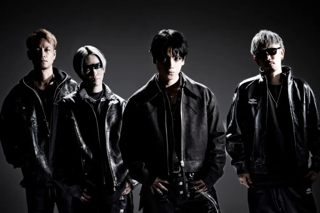 The four members of Japanese rock band SPYAIR standing side by side in black leather jackets against a dark grey studio backdrop, one wearing sunglasses and one with a black band painted across his eyes