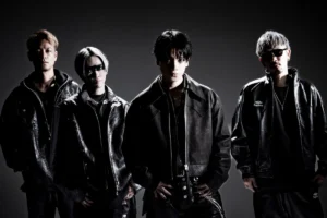 The four members of Japanese rock band SPYAIR standing side by side in black leather jackets against a dark grey studio backdrop, one wearing sunglasses and one with a black band painted across his eyes