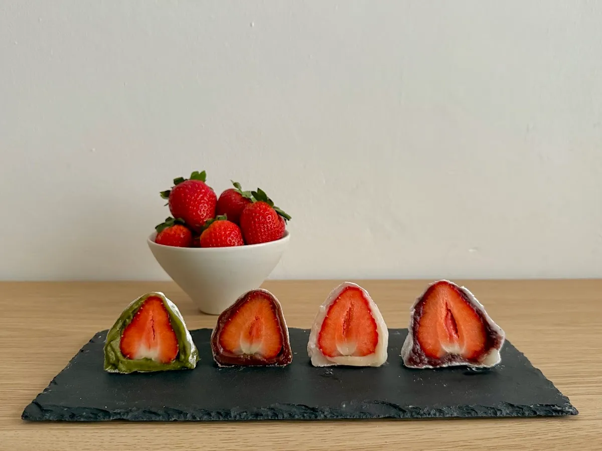 Four halved strawberry mochi on a slate board showing whole strawberries inside soft rice cake, with a bowl of strawberries behind